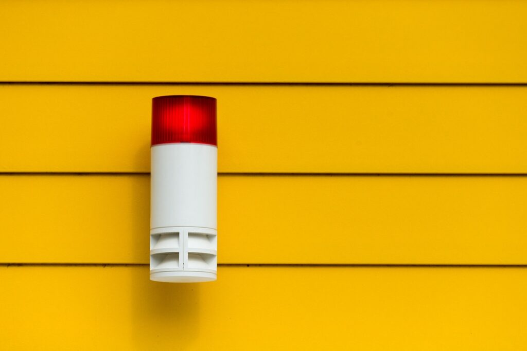 An einer gelben Hauswand ist eine Alarmanlage angebracht mit roter Signalleuchte.